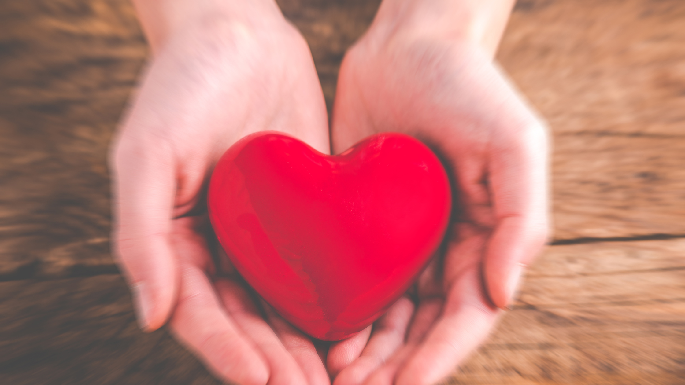 Hands holding a red heart symbolizing love, care, and charitable giving on a wooden background.