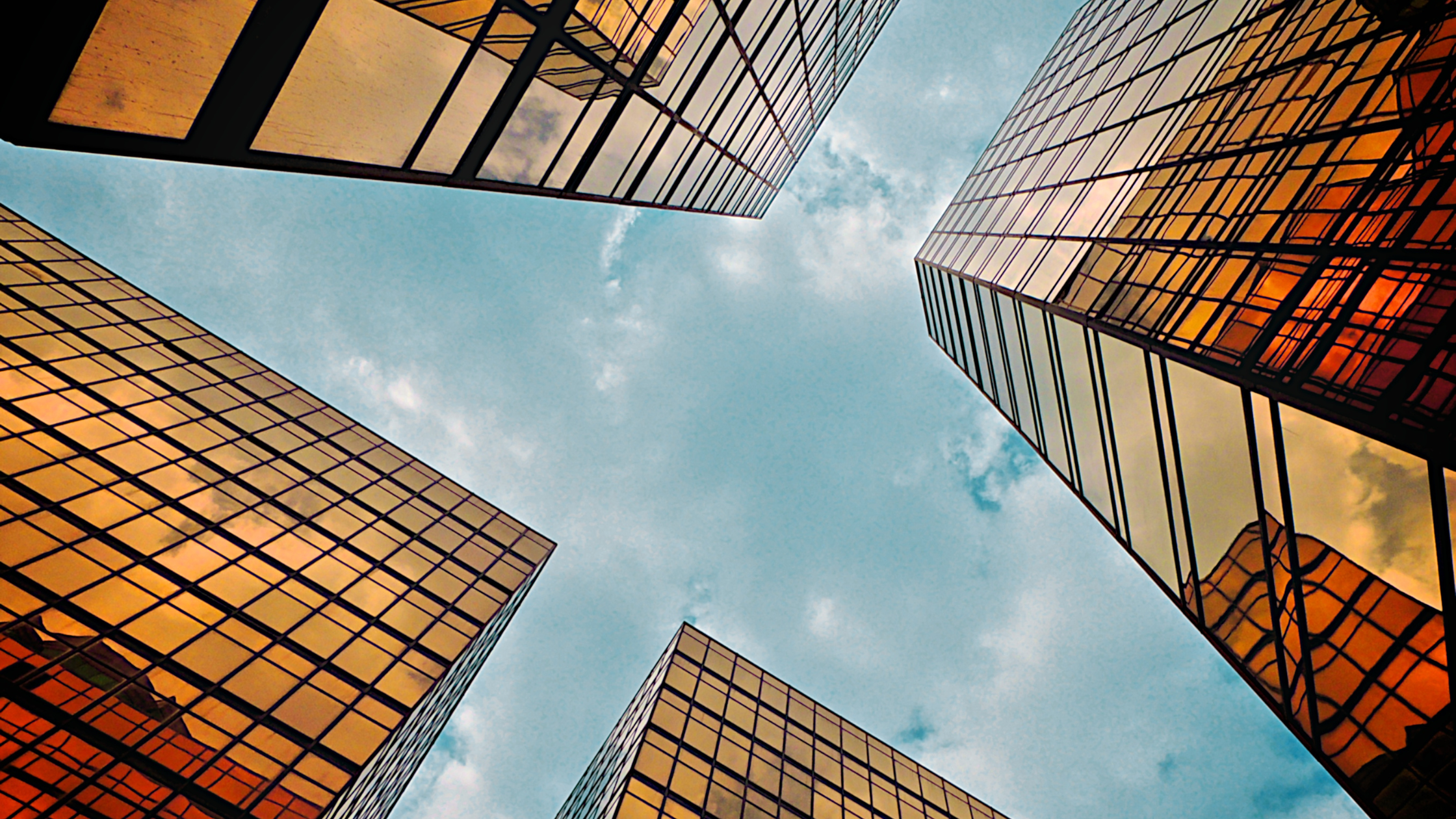 Upward view of four golden glass skyscrapers with blue sky in the center, symbolizing structure, clarity, and strategic perspective.