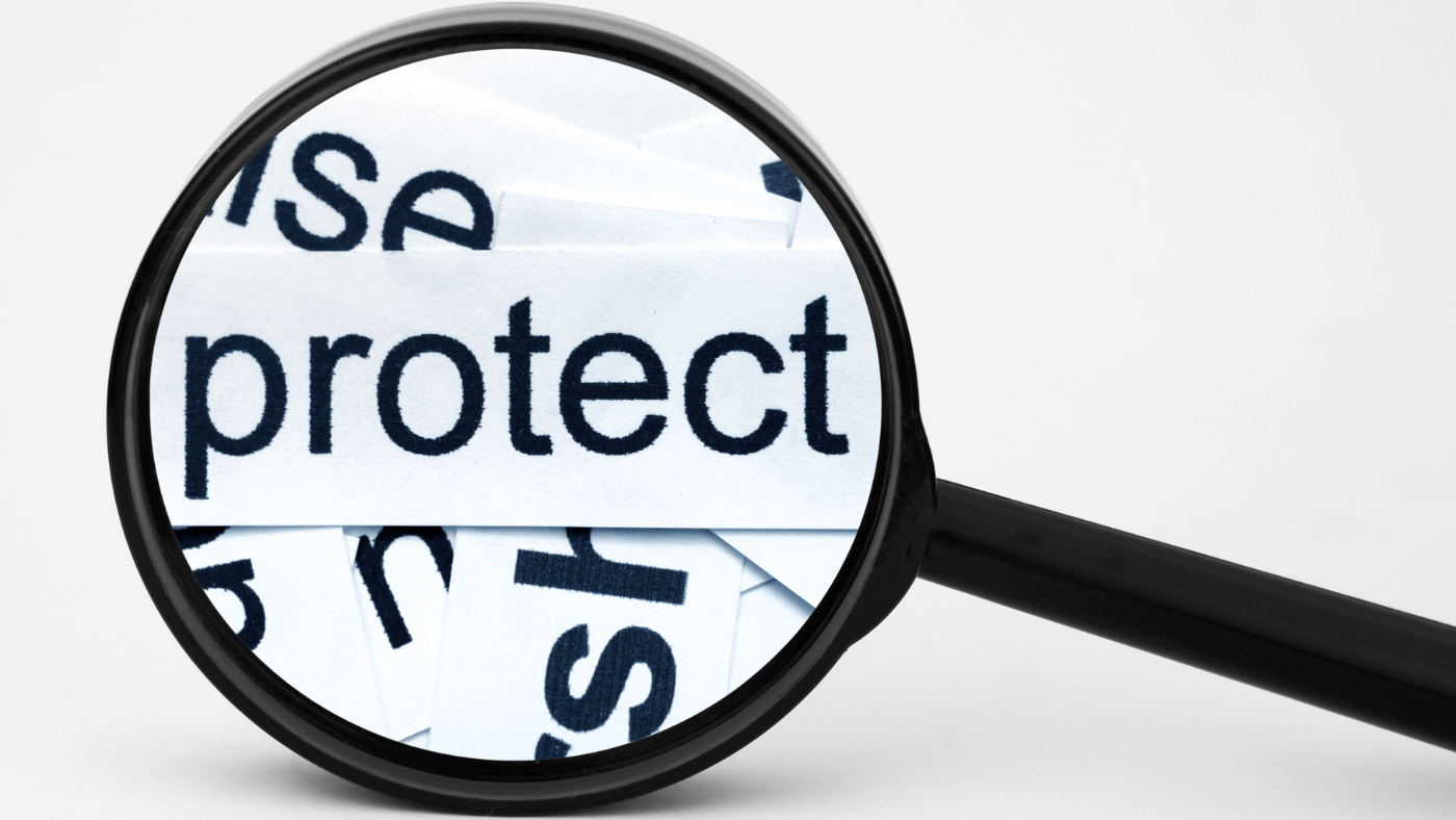 A magnifying glass highlighting the word "protect" printed on white paper, symbolizing the concept of protection, security, or scrutiny—commonly associated with identity theft prevention or data privacy.