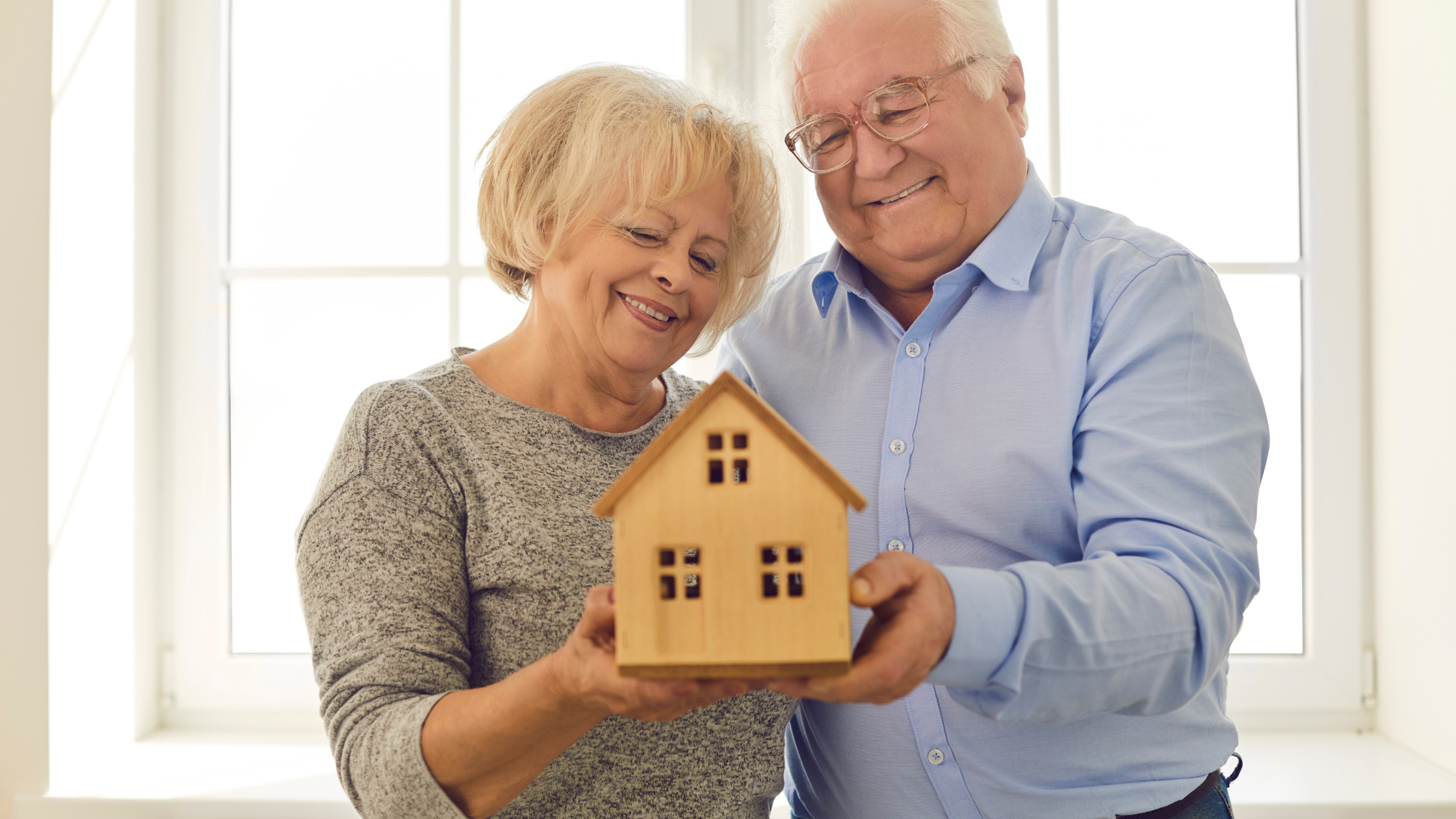 a retiree couple holding a wooden model of a simple home